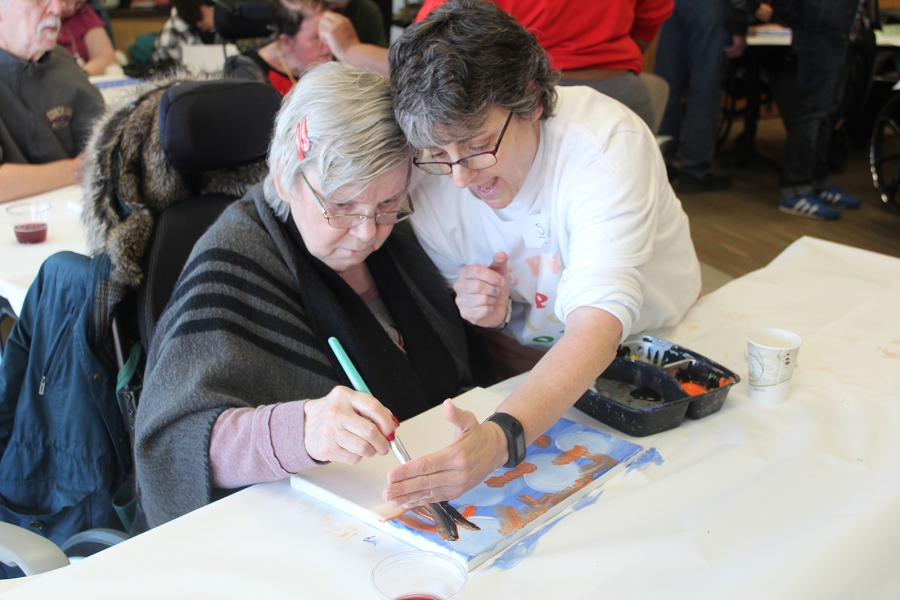A volunteer helps a client hold a pencil to draw a picture.