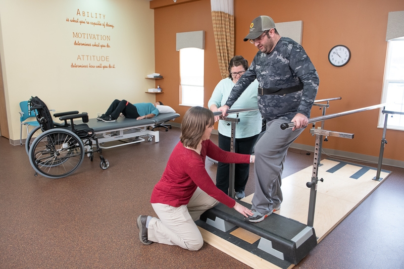 Physical therapist works with client in the gym on the paralell bars.
